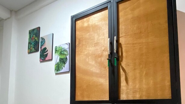 A room with a large wooden cabinet with glass doors, tiled floor, and three wall-mounted pictures. - Fi Hostel Kuta (Kuta)