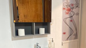 A bathroom with a white sink, wooden cabinet, and a decorative mirror. - Fi Hostel Kuta (Kuta)