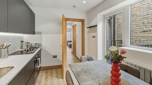 A modern kitchen with a built-in oven, a dining area with a table and chairs, and a window with a brick wall view. - Your London Escape | Stylish 3BR Apartment Stay (London)