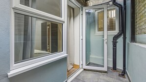 A corner of a building with a window, a door, and a black pipe. - Your London Escape | Stylish 3BR Apartment Stay (London)