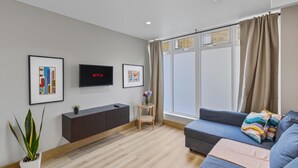 A modern living room with a grey sofa, a TV mounted on the wall, and a large window with curtains. - Your London Escape | Stylish 3BR Apartment Stay (London)
