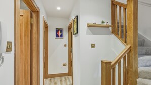 A hallway with wooden doors, a staircase with wooden railings, and a small shelf with decorative items. - Your London Escape | Stylish 3BR Apartment Stay (London)