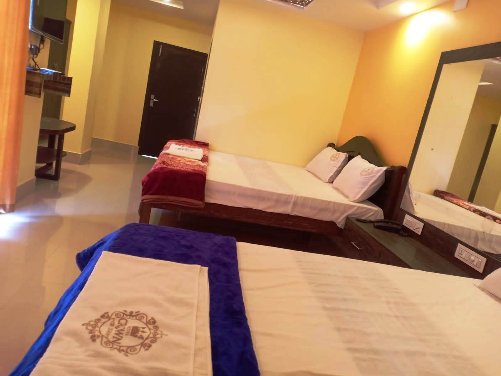 A hotel room with two beds, a small table, a chair, a TV, and a door.