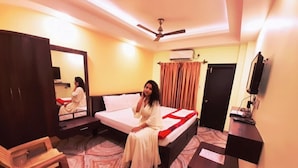 A hotel room with a bed, a desk, a chair, a mirror, and a ceiling fan. - Hotel Crown of Digha (Digha)