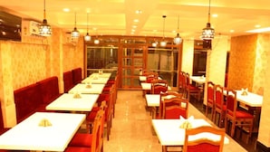 A restaurant with multiple tables and booths, arranged in a linear fashion with a central walkway. - Hotel Crown of Digha (Digha)