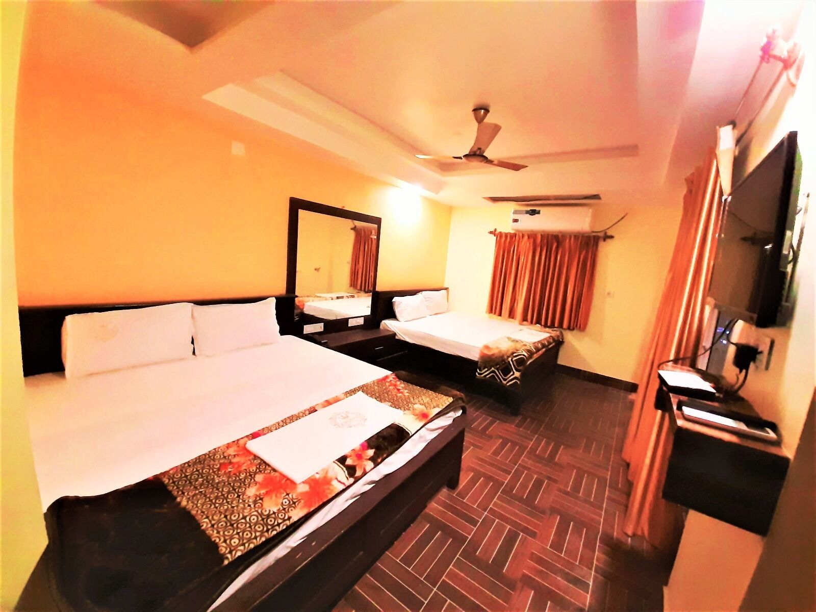 A hotel room with two beds, a ceiling fan, a TV, and an air conditioning unit.