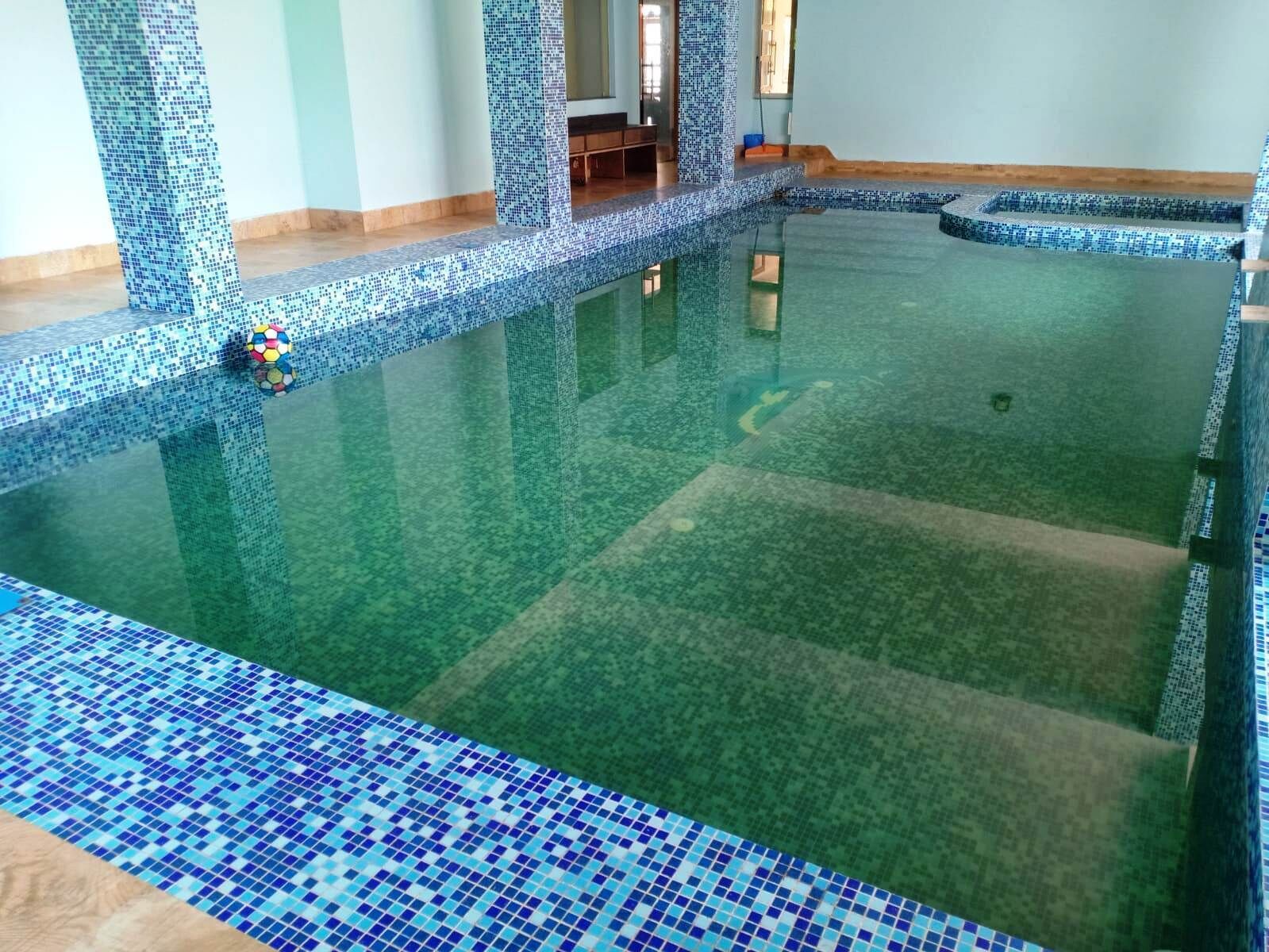 En inomhuspool med väggar beklädda med mosaik och ett blått kaklat golv.