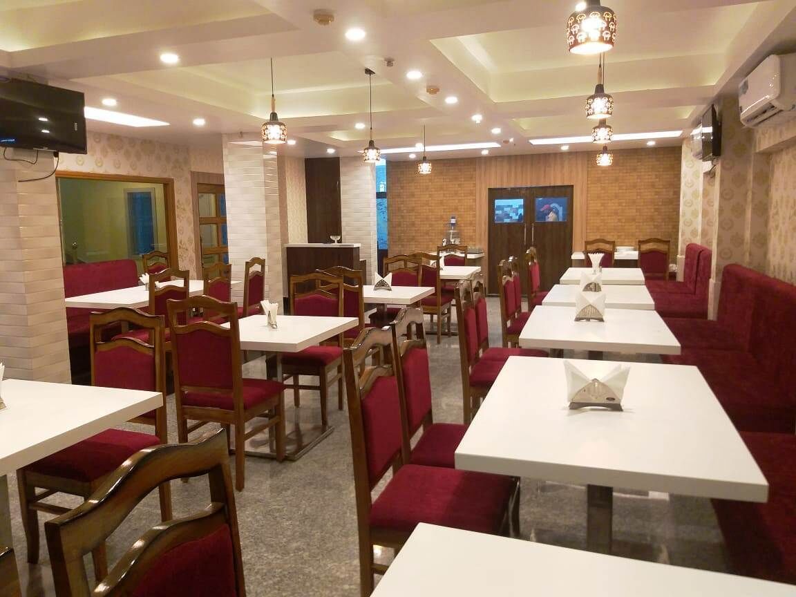 Ein Restaurant mit weißen Tischen, roten Sitzbänken, Holzhockern und hängenden Pendelleuchten.
