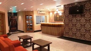 A lobby with a reception desk, a TV mounted on the wall, and a seating area with a sofa and a table. - Hotel Crown of Digha (Digha)