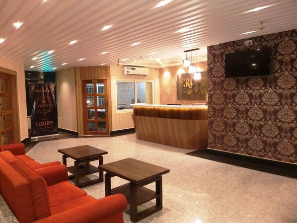 A lobby with a reception desk, a TV mounted on the wall, and a seating area with a sofa and a table.