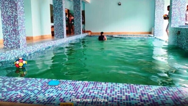 A swimming pool with mosaic tiles, a person swimming, and a view of the interior. - Hotel Crown of Digha (Digha)