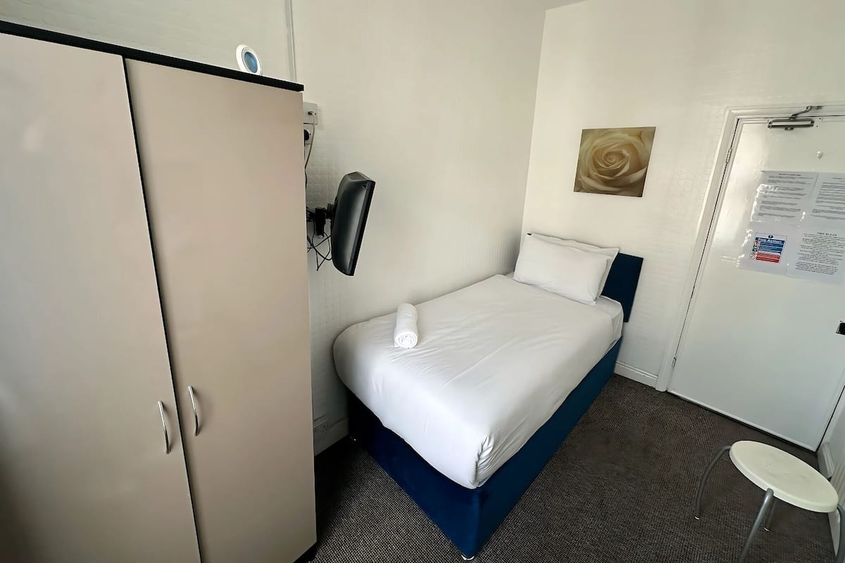 Habitación de hotel con cama, armario, un taburete pequeño y un calentador fijado a la pared.