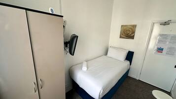 Habitación de hotel con cama, armario, un taburete pequeño y un calentador fijado a la pared.
