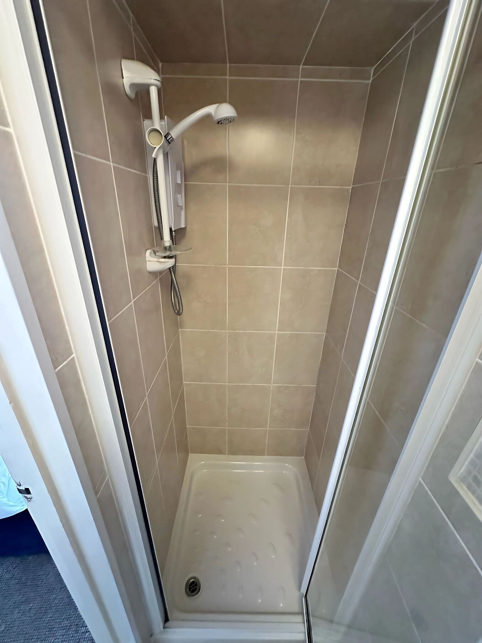 A small, enclosed shower area with a handheld showerhead and a wall-mounted control panel.