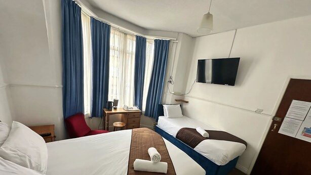 Et hotelværelse med to senge, et skrivebord, en stol, et fjernsyn og et vindue med gardiner.
