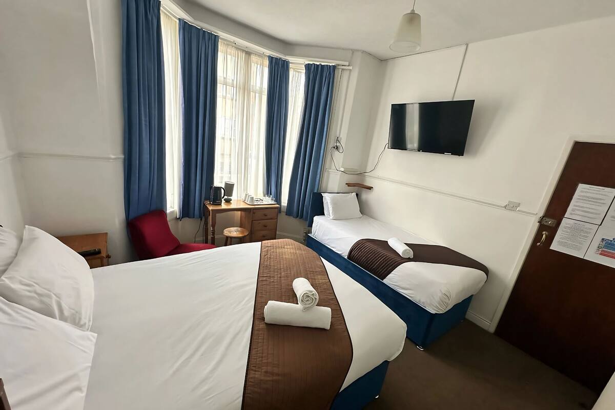 Habitación de hotel con dos camas, un escritorio, una silla, un televisor y una ventana con cortinas.