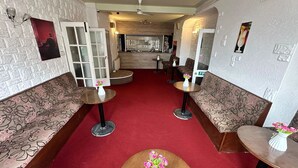 Et hotel lobby med rød løber, blomstermønstrede sofaer, runde borde med vaser og en væg af hvide mursten.