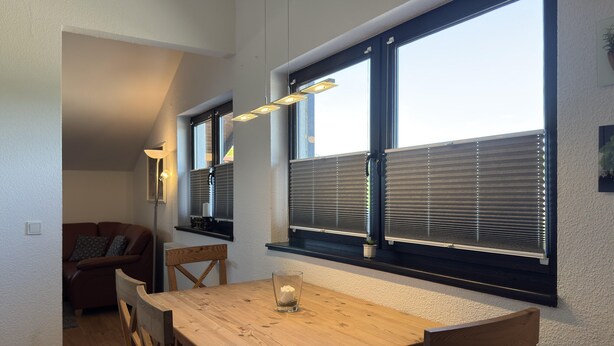 Ein Essbereich mit einem Holztisch und Stühlen, einer Kerze auf dem Tisch und einem Fenster mit Jalousien.