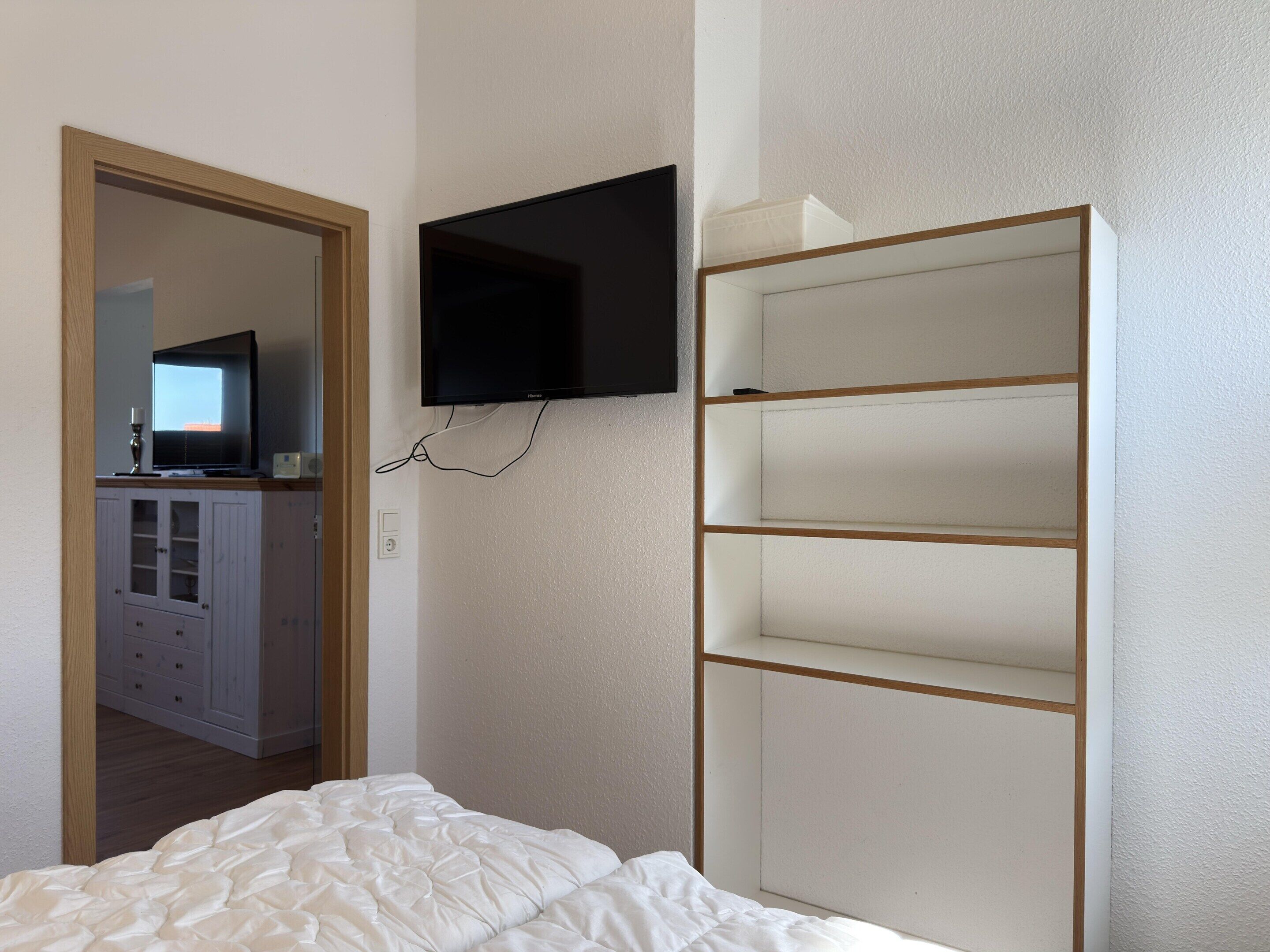A bedroom with a bed, a TV mounted on the wall, and a wardrobe with multiple shelves.