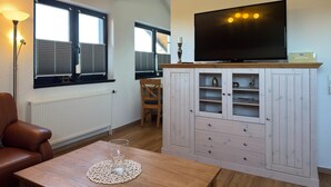 Ein Wohnzimmer mit Fernseher auf einer Holzkommode, einem Tisch mit einem Glas und einem Sessel.