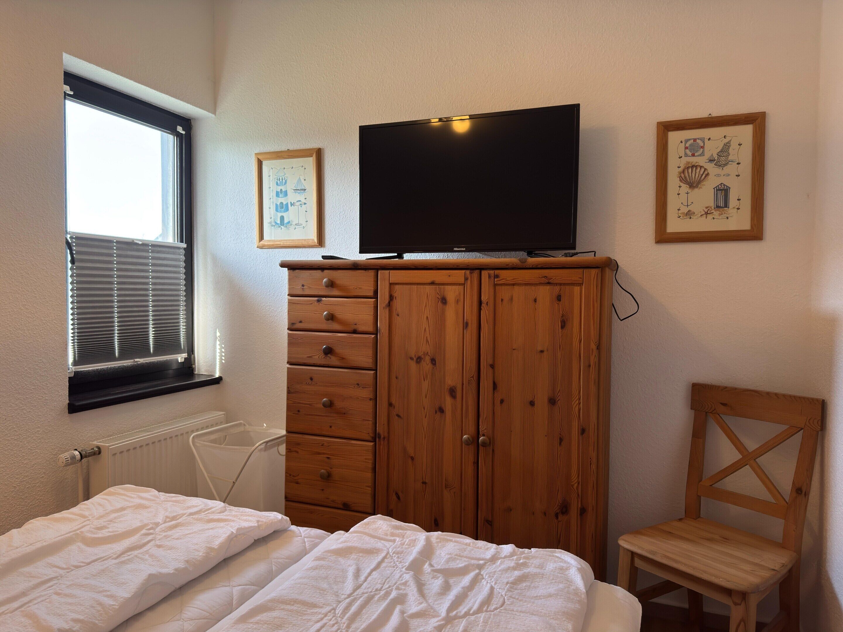 A bedroom with a bed, a wooden wardrobe, a television, and a chair.