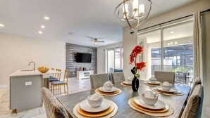 Un'area pranzo moderna con un tavolo lungo apparecchiato per sei persone, una zona cucina e un'ampia finestra con vista sull'esterno.