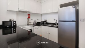 A modern kitchen with white cabinets, a stainless steel refrigerator, a black countertop, and a microwave. - Manzil -1BR w Pool nr Dubai Sports City  (Dubai)