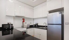 A modern kitchen with white cabinets, a stainless steel refrigerator, a black countertop, and a microwave. - Manzil -1BR w Pool nr Dubai Sports City  (Dubai)