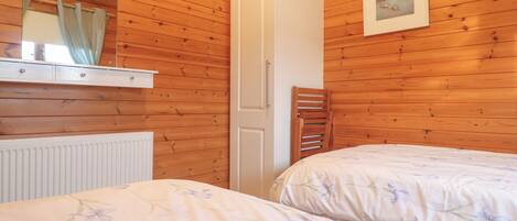 A bedroom with wooden panel walls, a white wardrobe, two beds with floral bedding, a radiator, and a framed picture on the wall.