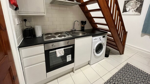 A compact kitchen with a stove, oven, sink, and washing machine. A wooden staircase leads to an upper level. - Modern Studios Malvern Road  (London)