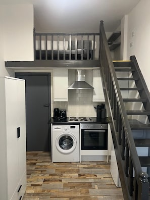 A compact kitchen with a washing machine, oven, and coffee maker.