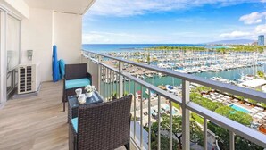 A balcony with wicker furniture, a view of a marina, and a clear sky. - Ocean & marina view w/ steps to Waikiki Beach (Honolulu)
