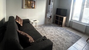 Uma sala de estar com um sofá, um quadro, uma televisão e uma janela.