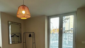 Quarto com cama, luminária pendente, janela com vista para edifícios e radiador.