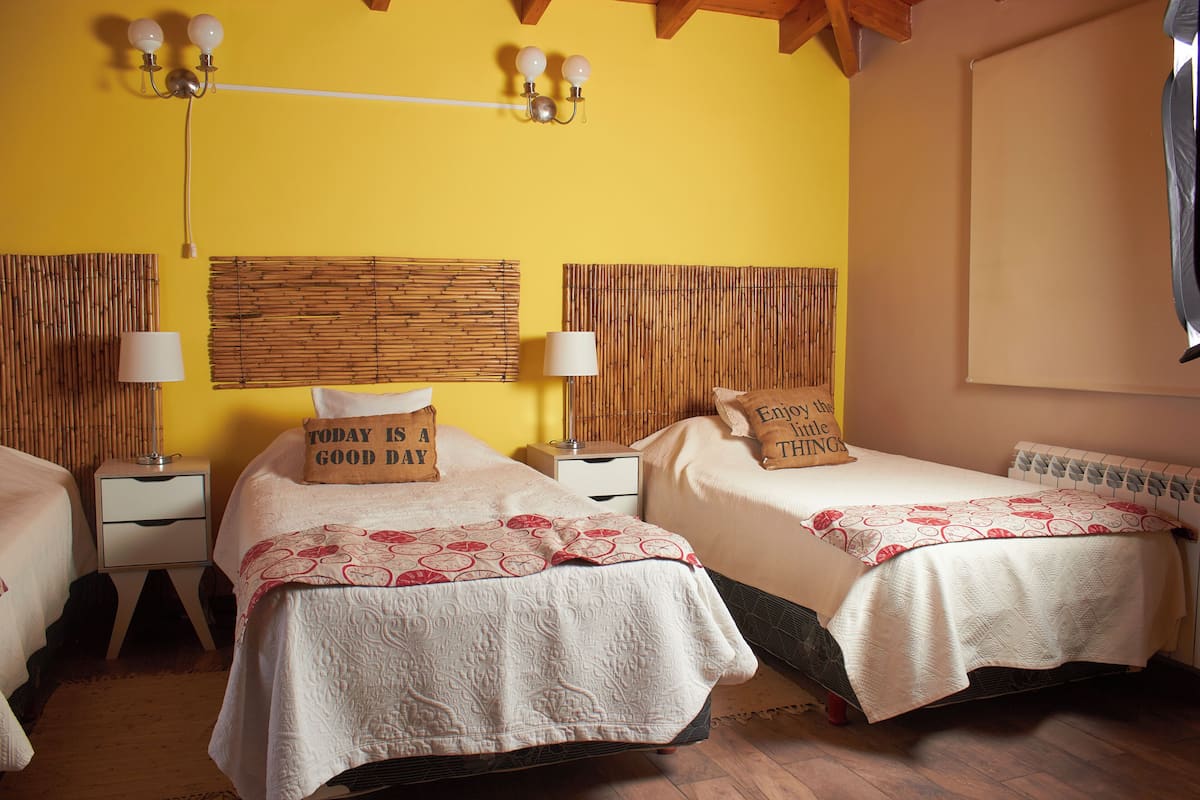 A hotel room with two beds, each with a pillow that reads "Today is a good day," and a wall-mounted lamp between them.