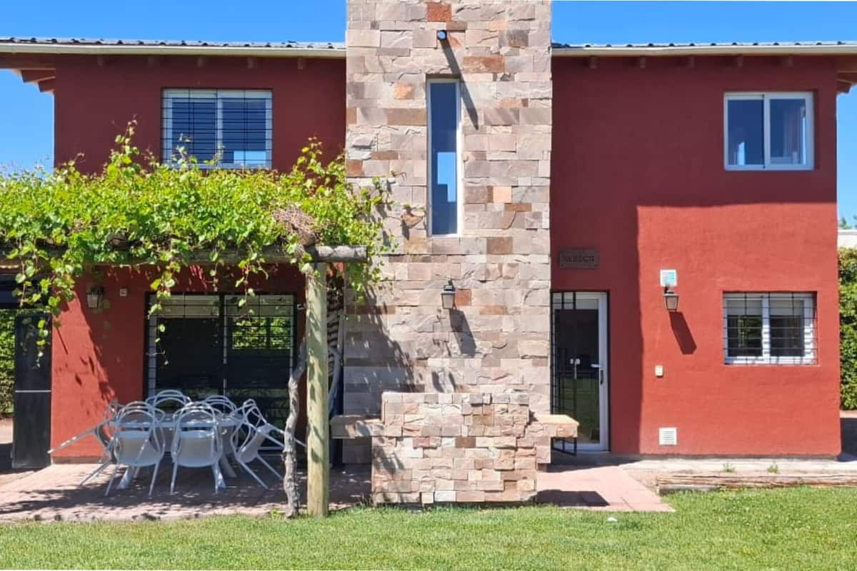 A two-story building with a red facade, stone pillar, and a pergola with vines.