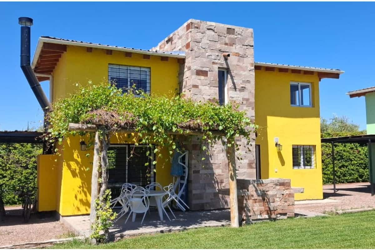 A yellow house with a stone tower, a pergola with climbing plants, and outdoor seating.