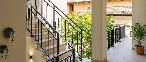 A staircase with black railings leading to a covered outdoor area with tiled flooring and potted plants.