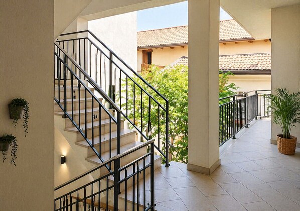 A staircase with black railings leading to a covered outdoor area with tiled flooring and potted plants. - Giulio Collio Suite House (Cormons)