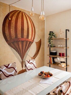 A dining area with a table set for two, a hot air balloon mural, and a bookshelf with various items.