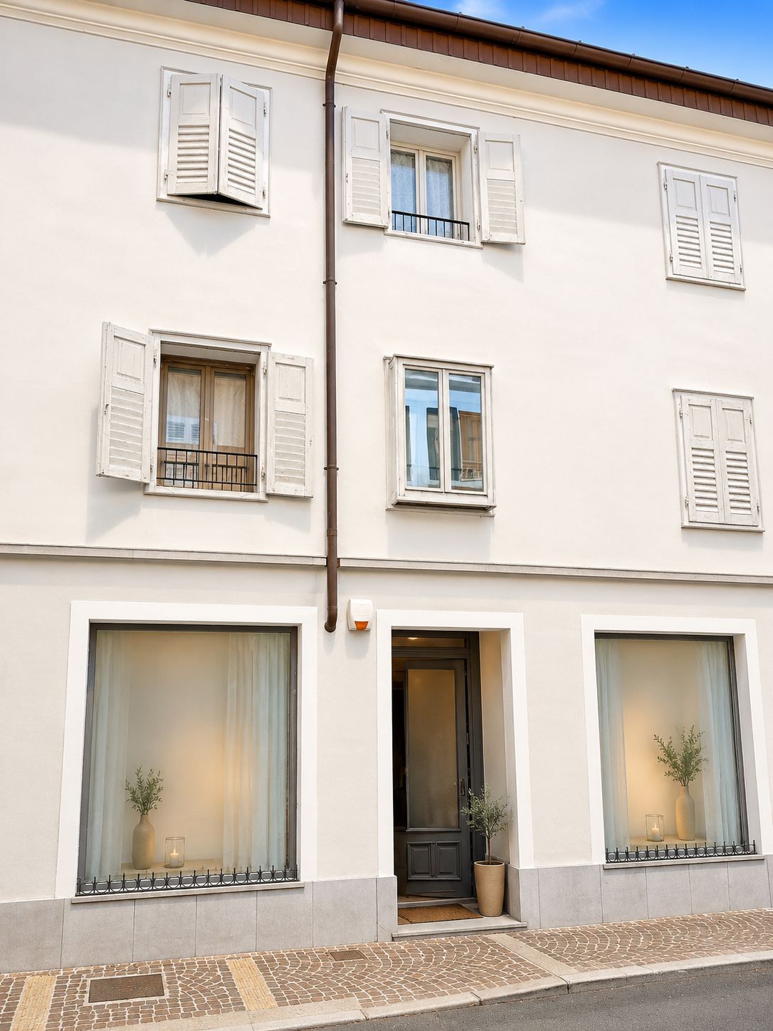 Un bâtiment à deux étages avec des murs blancs, de nombreuses fenêtres dotées de volets et une porte devant laquelle se trouve un pot de fleurs.
