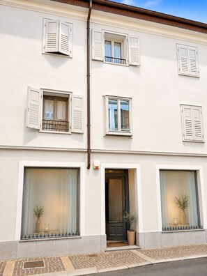 A two-story building with white walls, multiple windows with shutters, and a door with a potted plant outside. - Giulio Collio House Suite (Cormons)