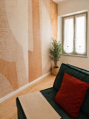 A room with a green sofa, a red pillow, a potted plant, and a window with curtains.