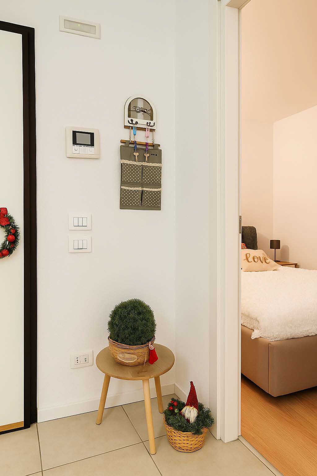 Une chambre avec un lit, une petite table sur laquelle est posée une plante, un luminaire fixé au mur et un thermostat.