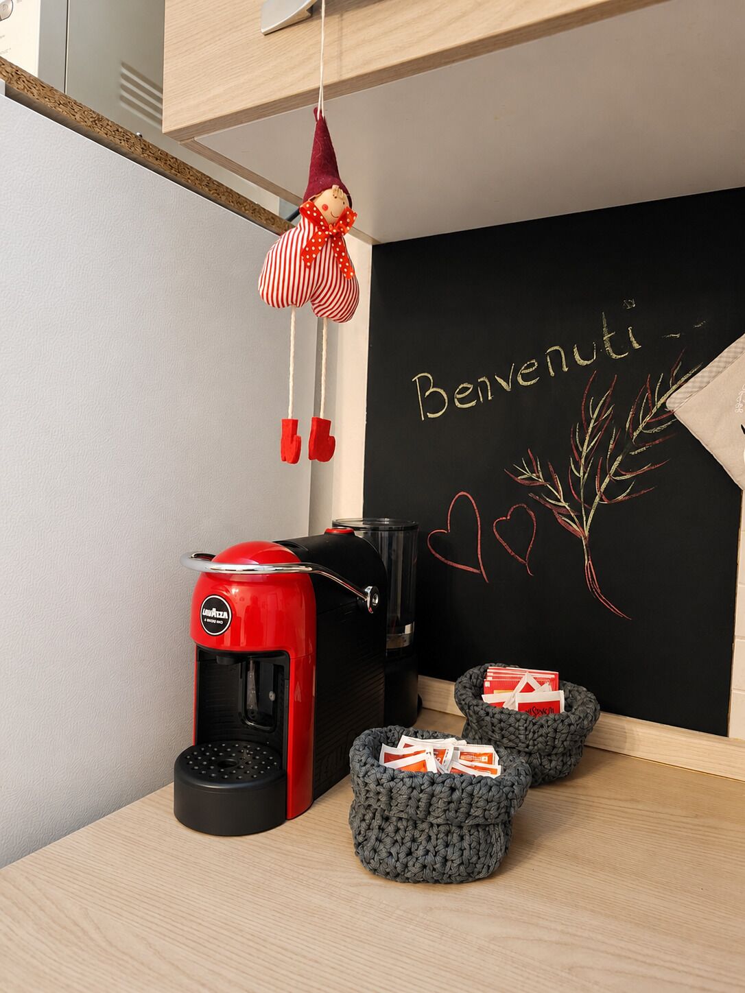 Een kitchenette met een rode koffiezetapparaat, een zwarte prullenbak en een schoolbord met 'Bienvenue' en een harttekening.