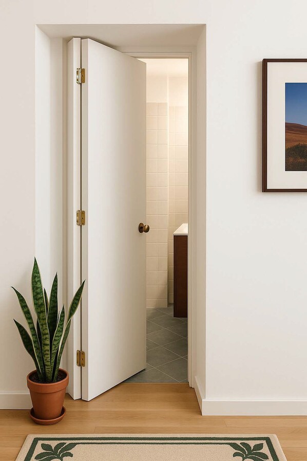 Un couloir avec une porte blanche, une plante en pot et un tableau encadré accroché au mur.