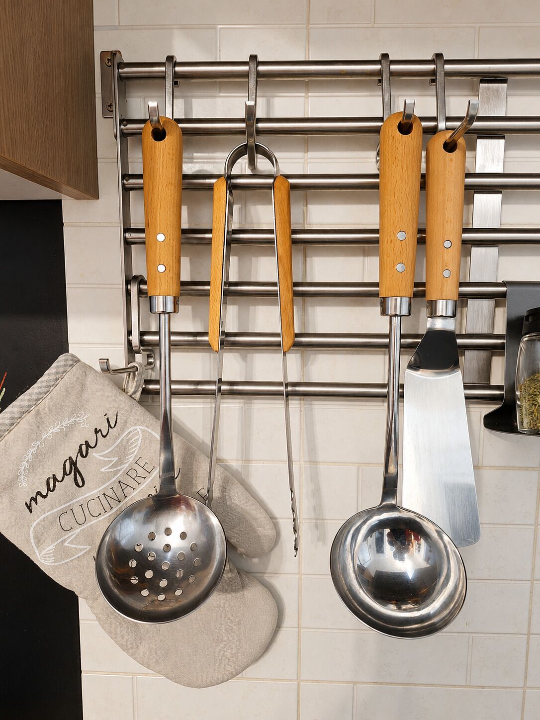 A kitchen with a hanging rack holding three wooden-handled utensils and two metal kitchen tools.