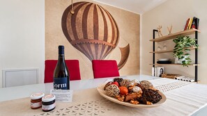 A dining table with a bottle of Corm wine, a plate of assorted food items, and a decorative wall mural. - Giulio Collio House Suite (Cormons)