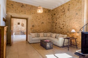 Une pièce avec un mur en pierre, un canapé, une malle en bois, une lampe et un téléviseur.