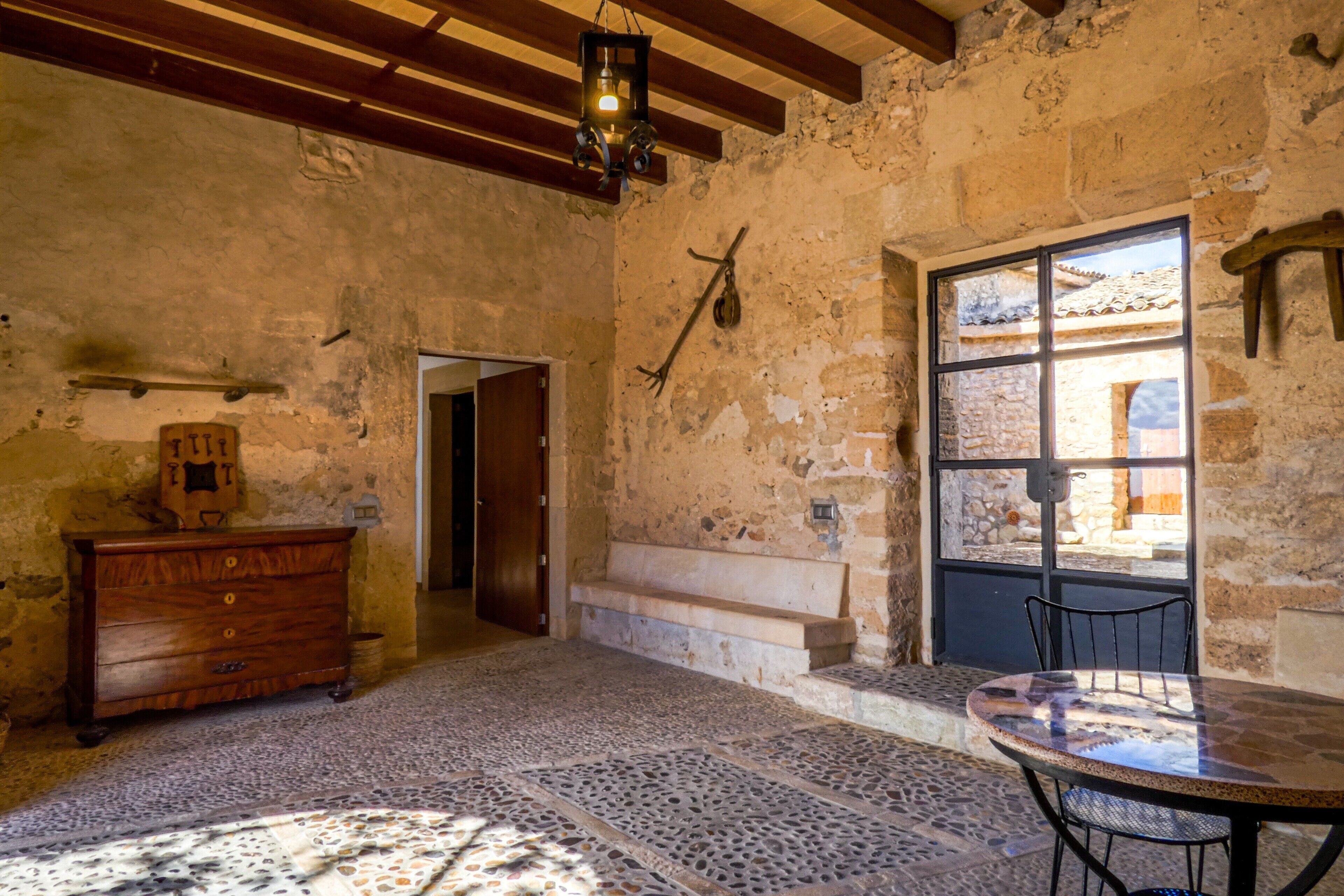 A rustic room with a stone wall, a wooden dresser, a bench, and a table with chairs.